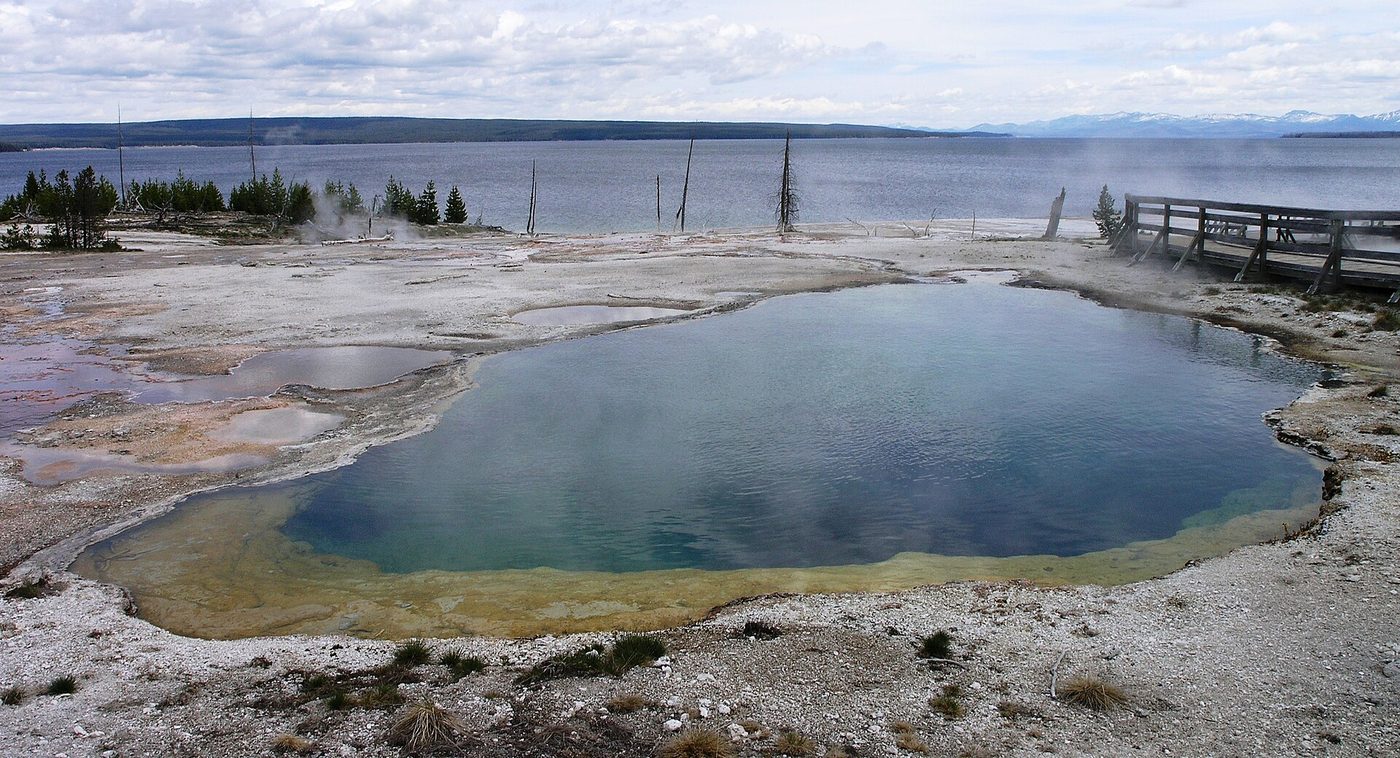 Deep blue Abyss Pool beside a boardwalk with Yellowstone Lake behind