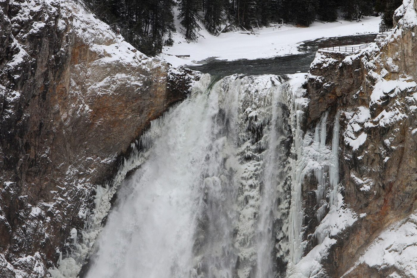 Snow and ice around a waterfall pouring into a frozen gorge in December