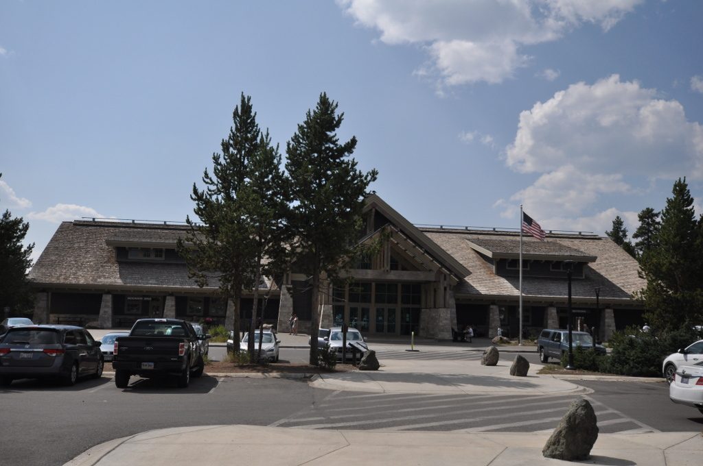 Stone and timber visitor center building with parked cars under a blue sky