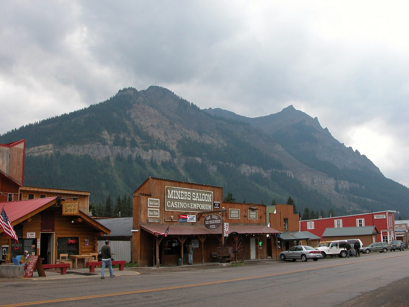Wooden storefronts including the Miners Saloon on the main street of Cooke City below a mountain