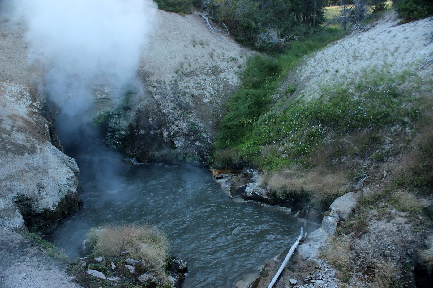 Steam and muddy water surging from a rock cave at Dragon's Mouth Spring