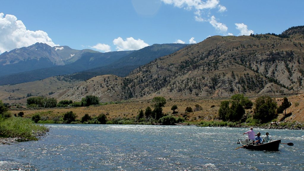 A drift boat on the Yellowstone River below dry hills with Electric Peak beyond