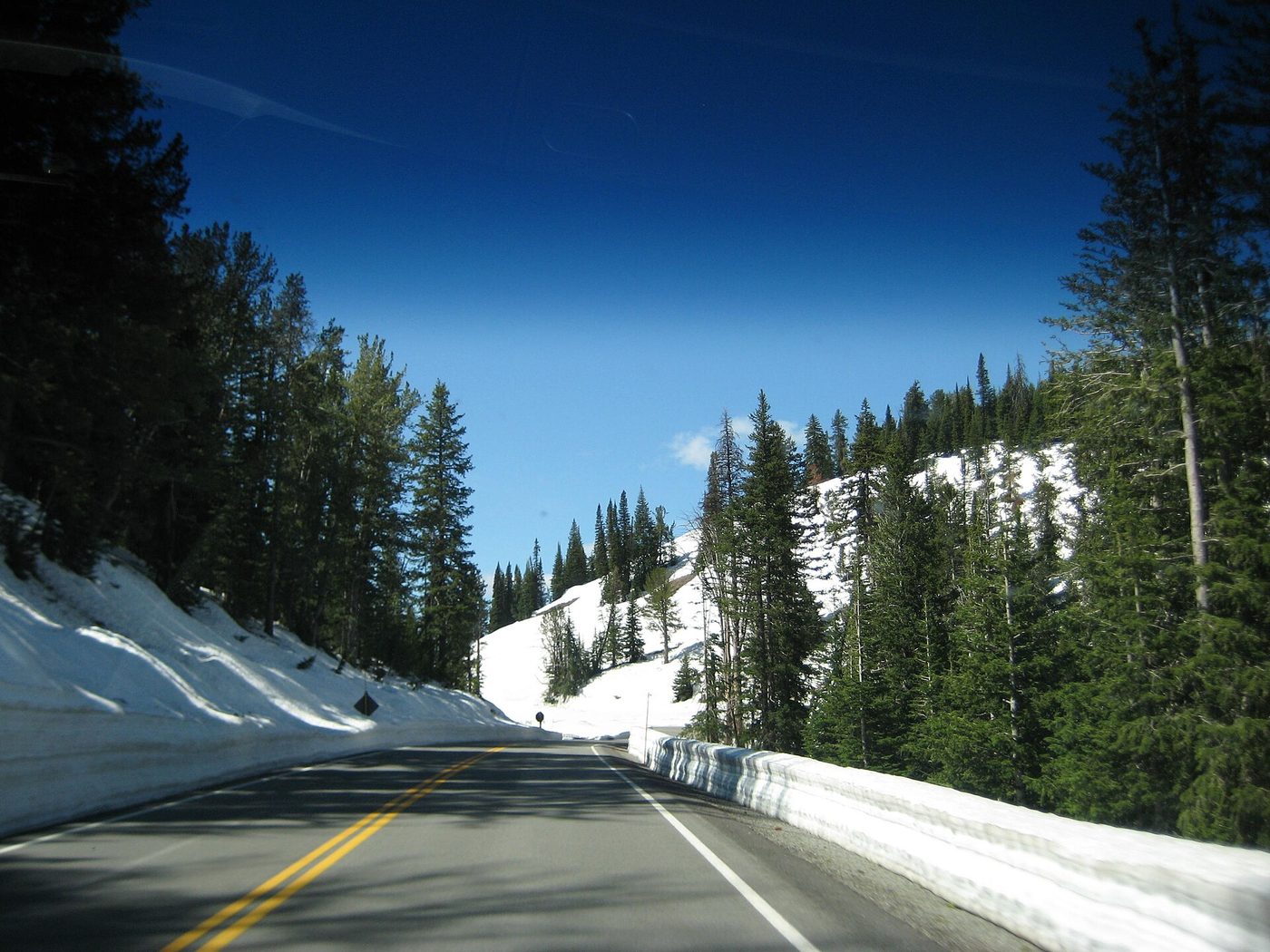 Snowbanks piled beside a clear lane of the Grand Loop Road at Dunraven Pass