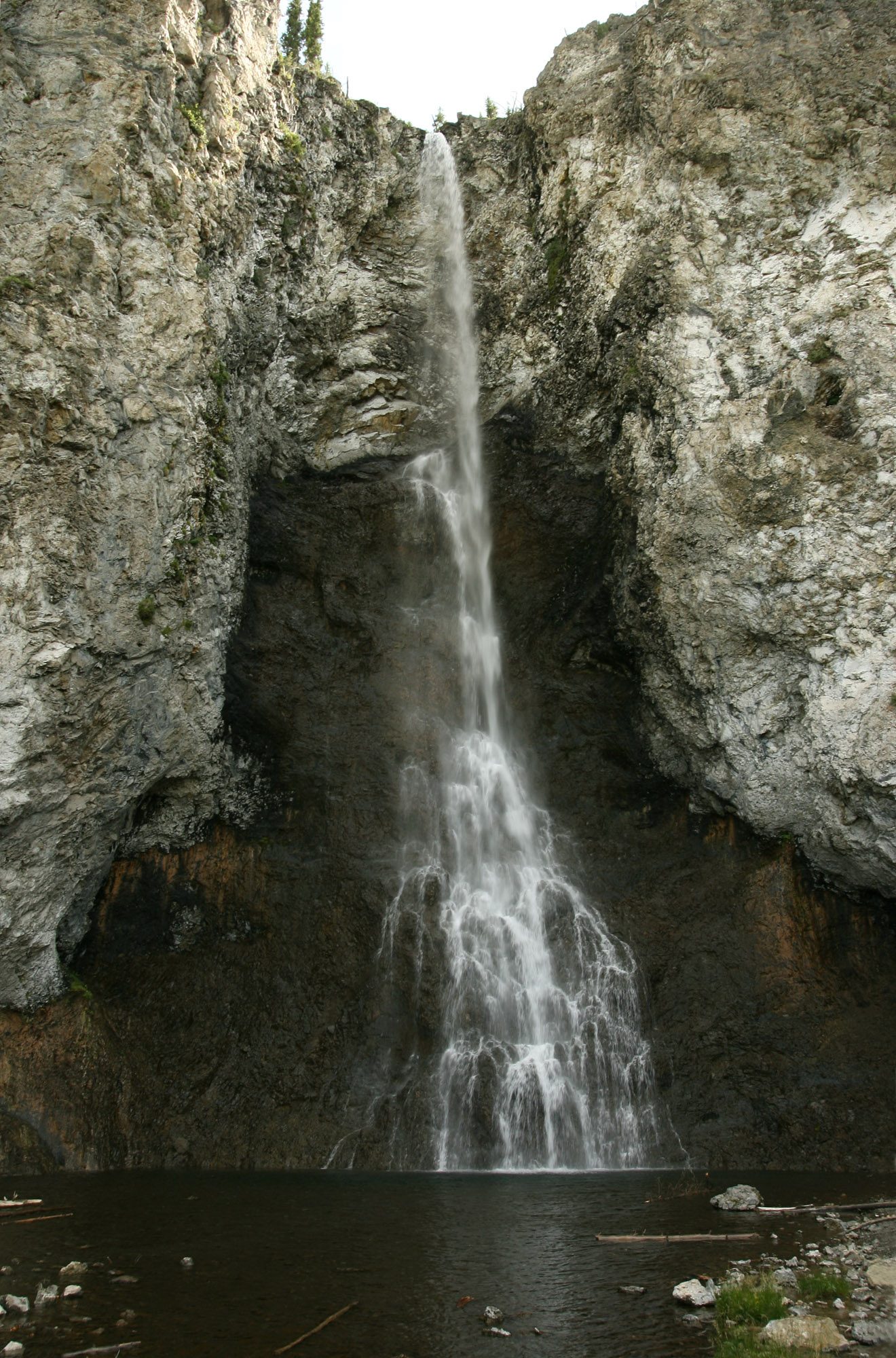 A narrow waterfall dropping down a gray cliff into a pool