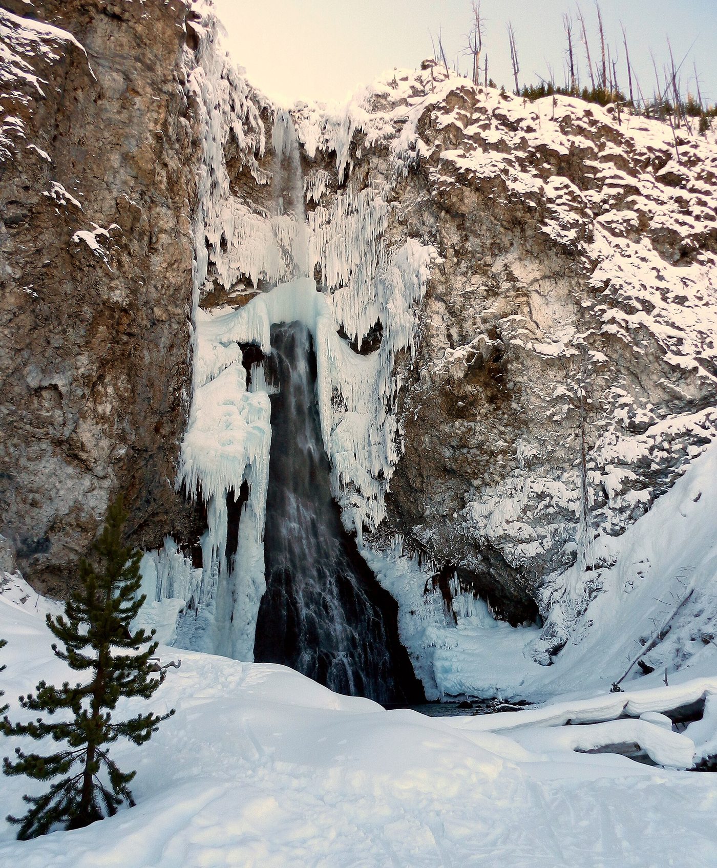 A waterfall partly frozen into columns of ice between snowy cliffs