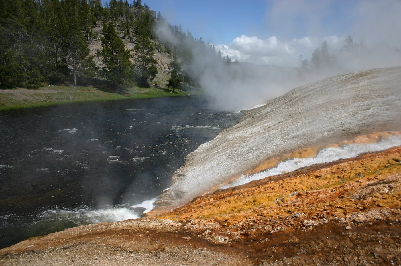 Steaming thermal runoff pouring over orange sinter into the Firehole River