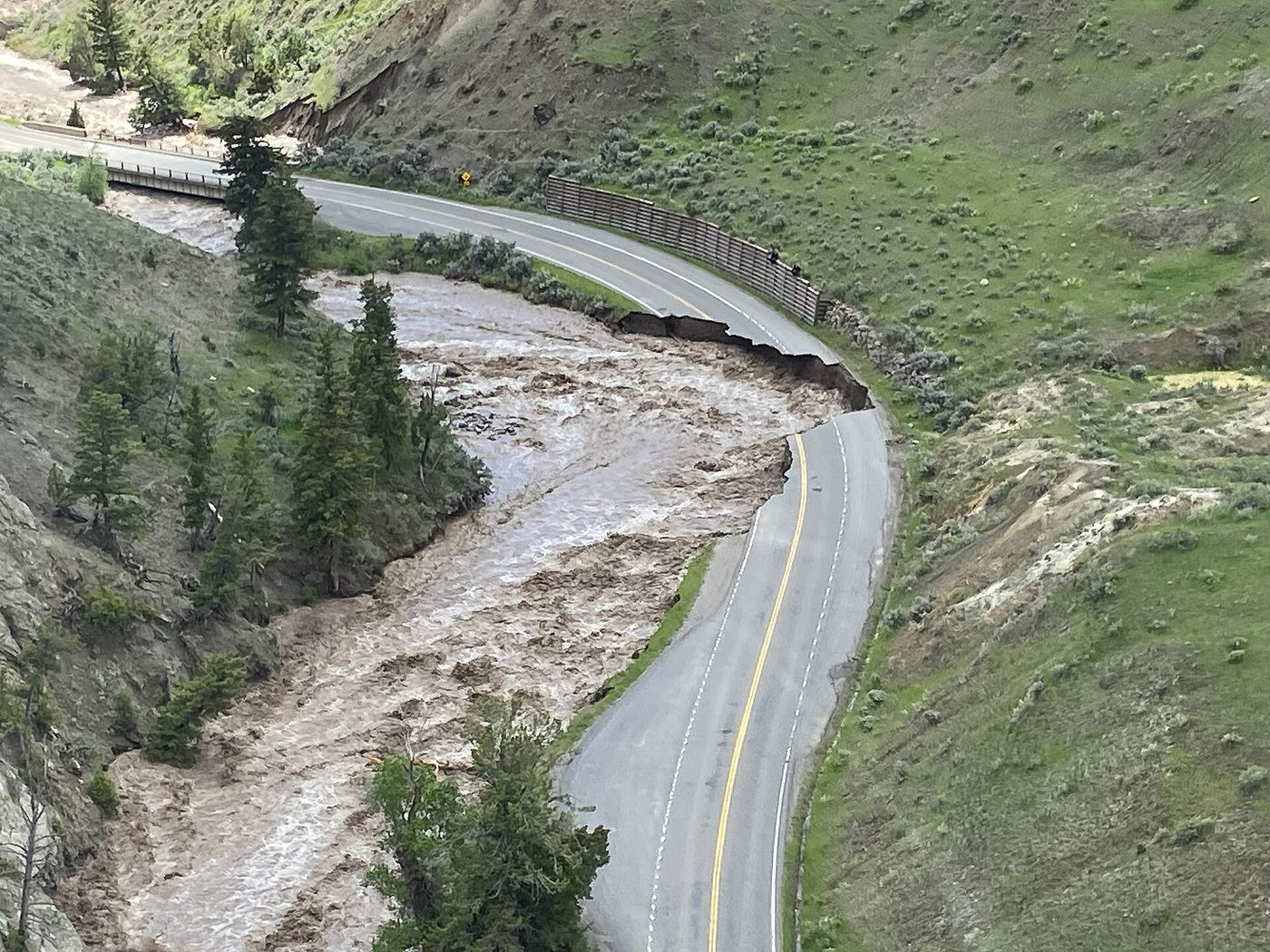 Aerial view of a flooded brown river eating into a road through a canyon