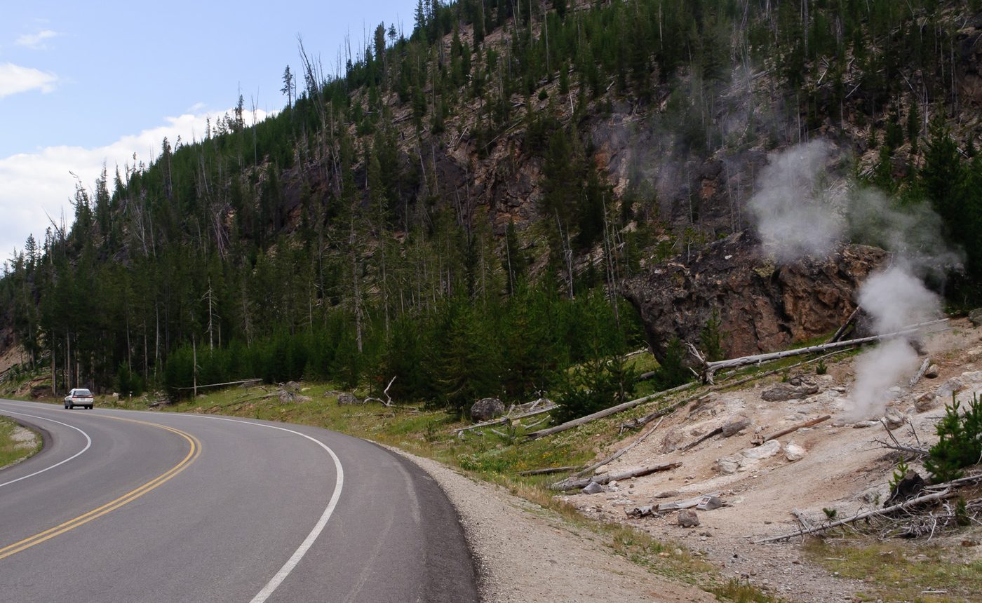 The Grand Loop Road curving past a steaming hillside in Yellowstone