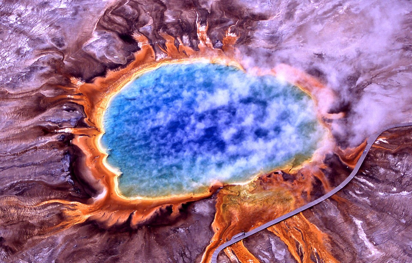 Aerial view of a huge blue hot spring with bright orange microbial mats radiating outward
