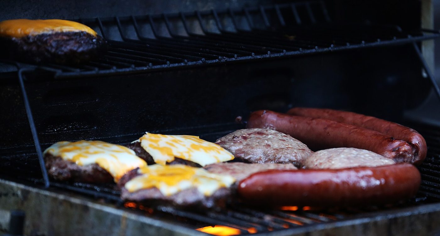 Burgers and sausages cooking over an open grill