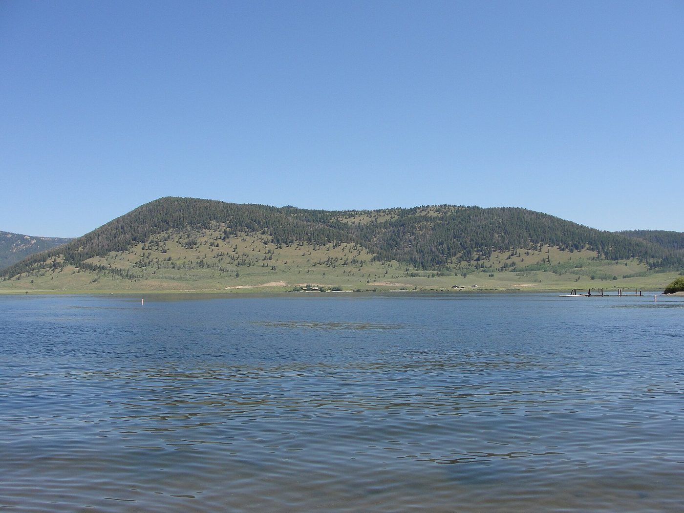 Calm blue water of Hebgen Lake seen from Rainbow Point with grassy hills beyond