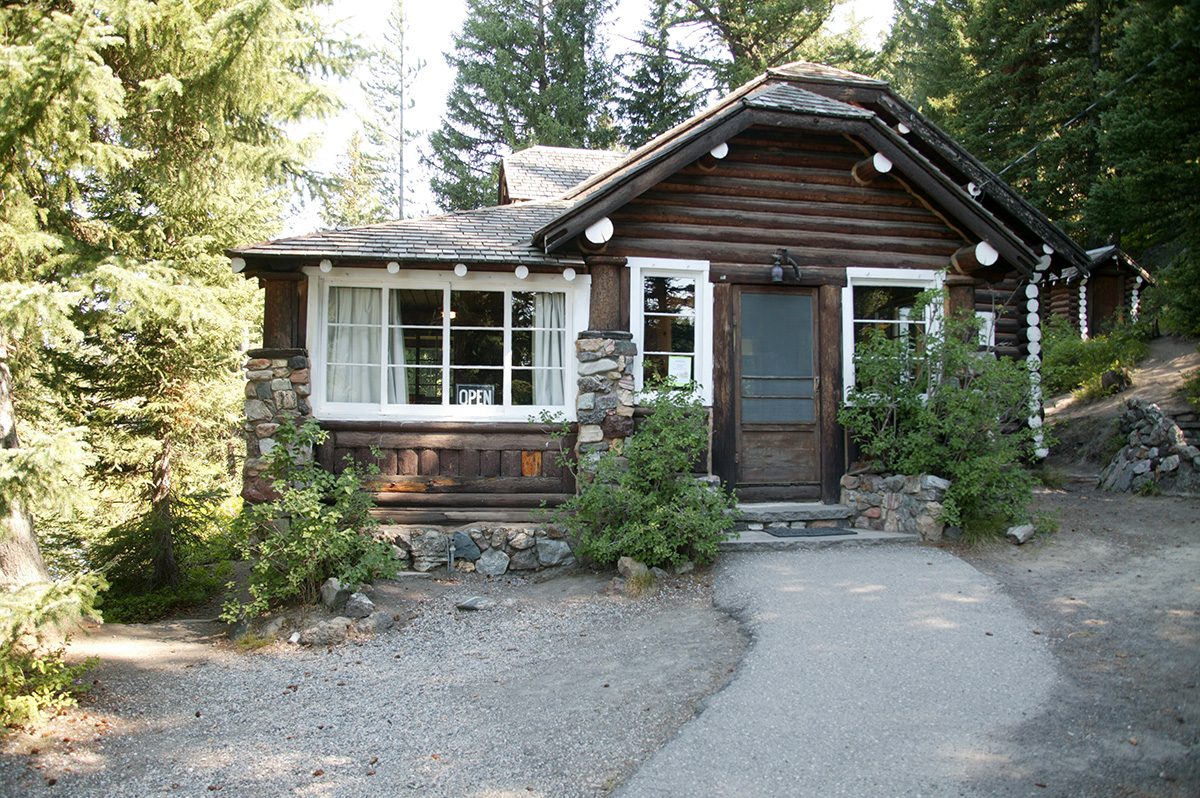 A small log cabin with stone trim and white-framed windows among trees at Big Springs