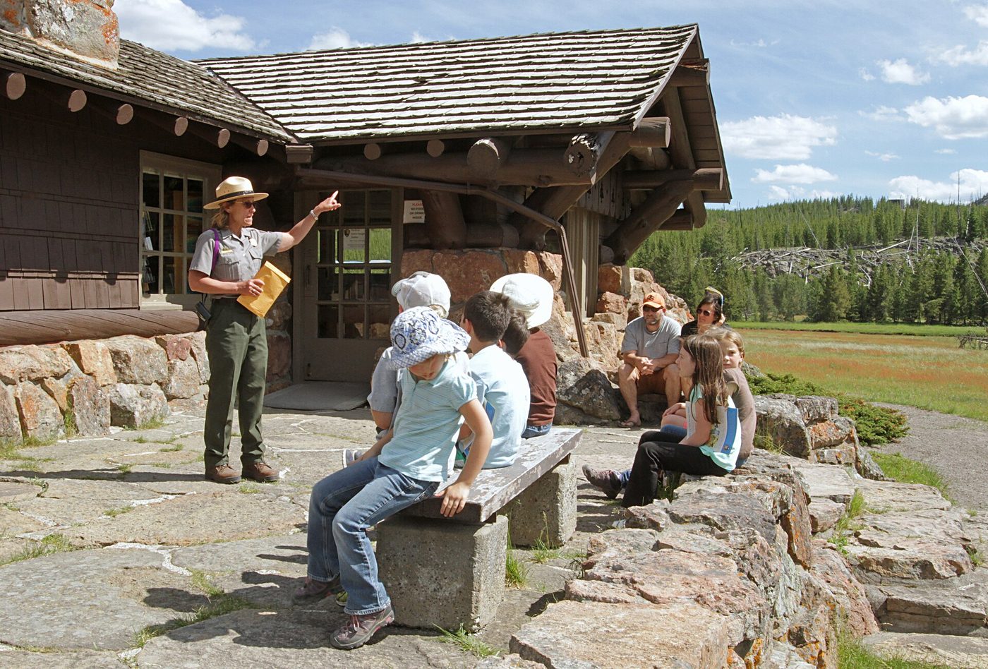 A ranger leading a Junior Ranger session with families seated outside a log ranger station