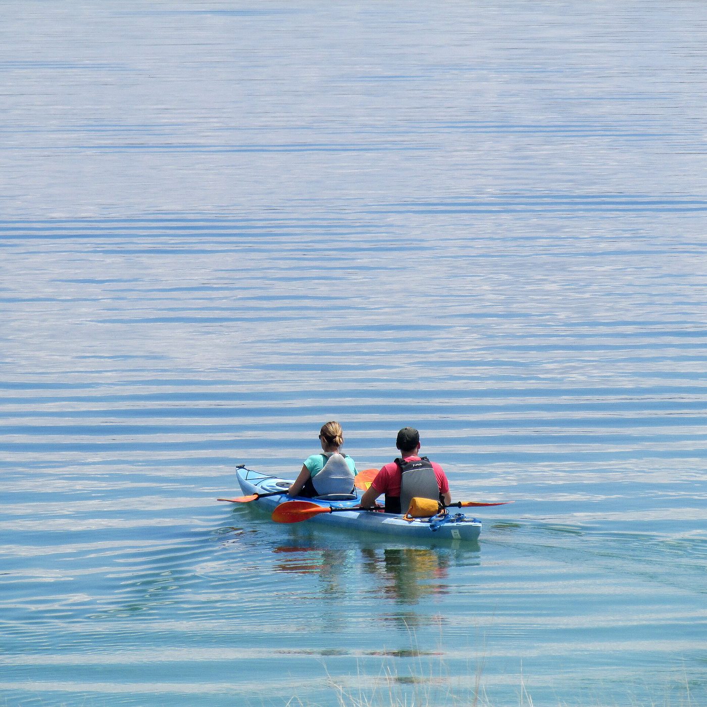 Two kayakers paddling across the flat blue water of Yellowstone Lake