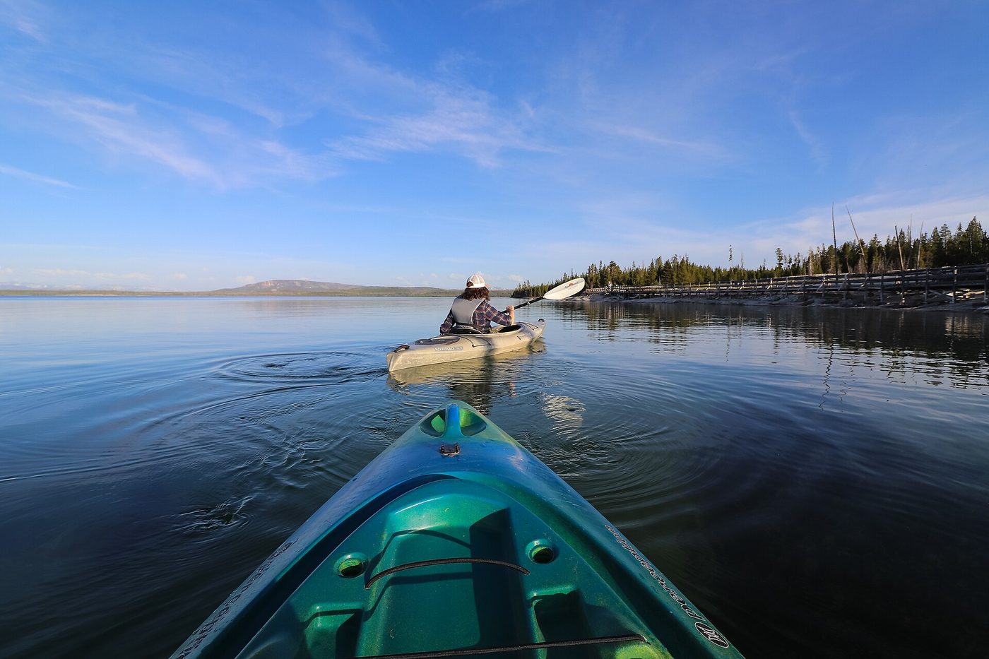 View from a kayak bow toward another paddler on calm blue lake water