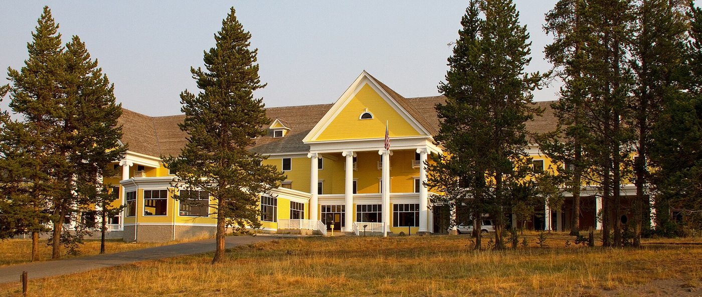 The pale yellow Lake Yellowstone Hotel with white columns behind a row of pines