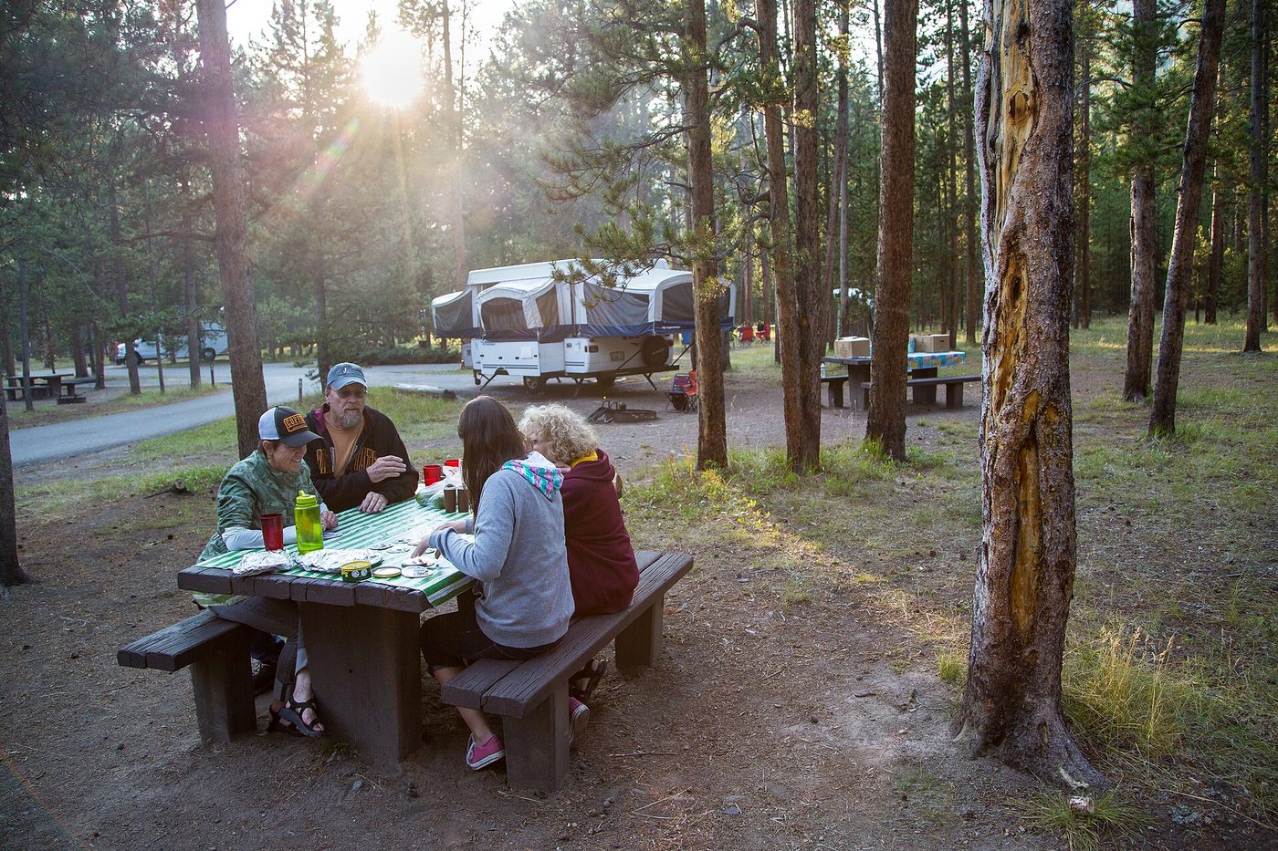A family sitting at a picnic table in early morning light at Madison Campground with RVs behind them
