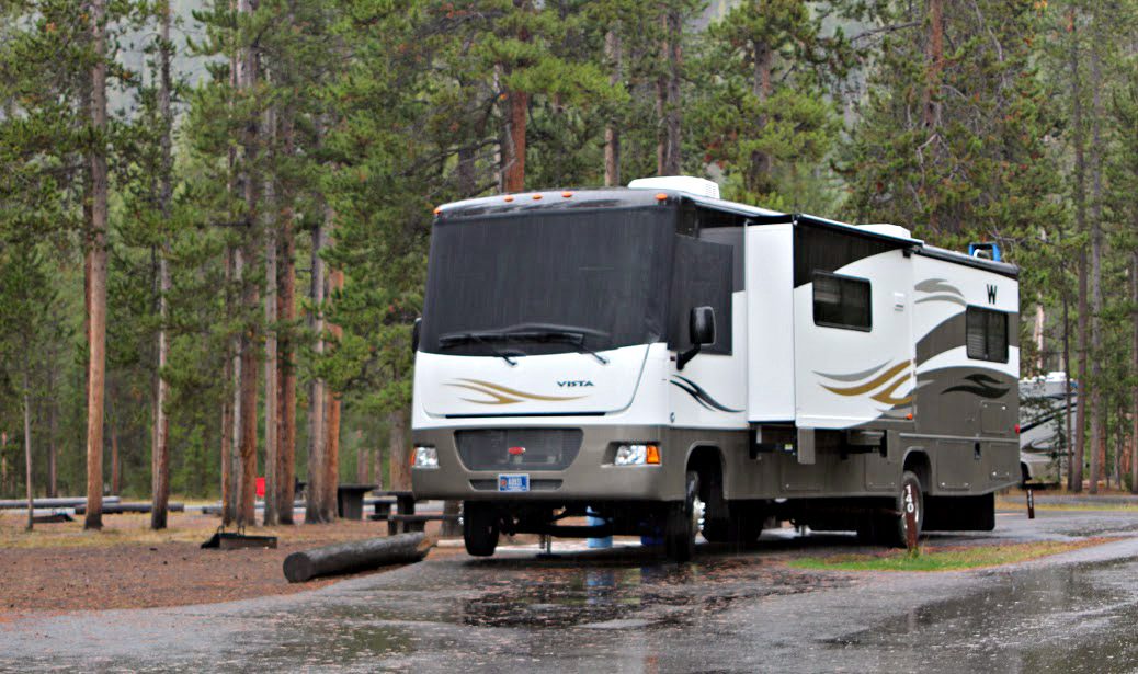 Large motorhome parked at a forested site after rain