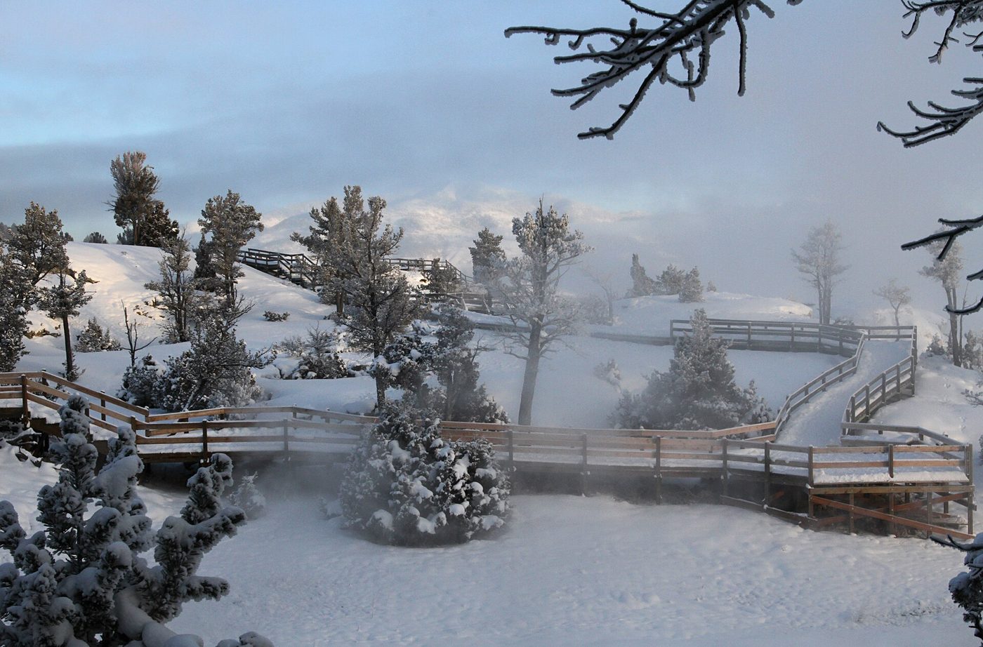 Snow-covered boardwalks winding through steaming terraces and frosted trees