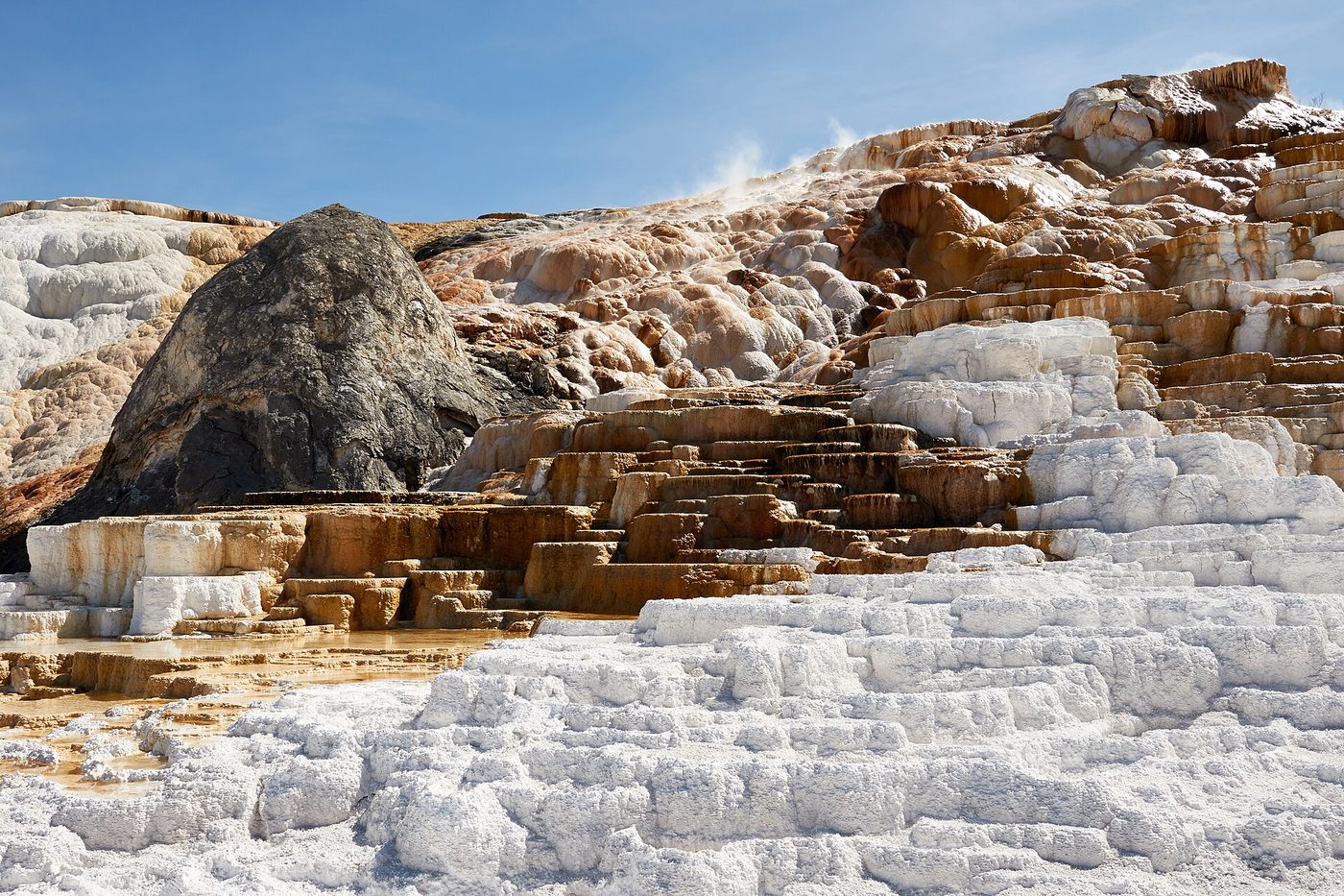 White and orange travertine terraces stepping down the hillside at Mammoth Hot Springs