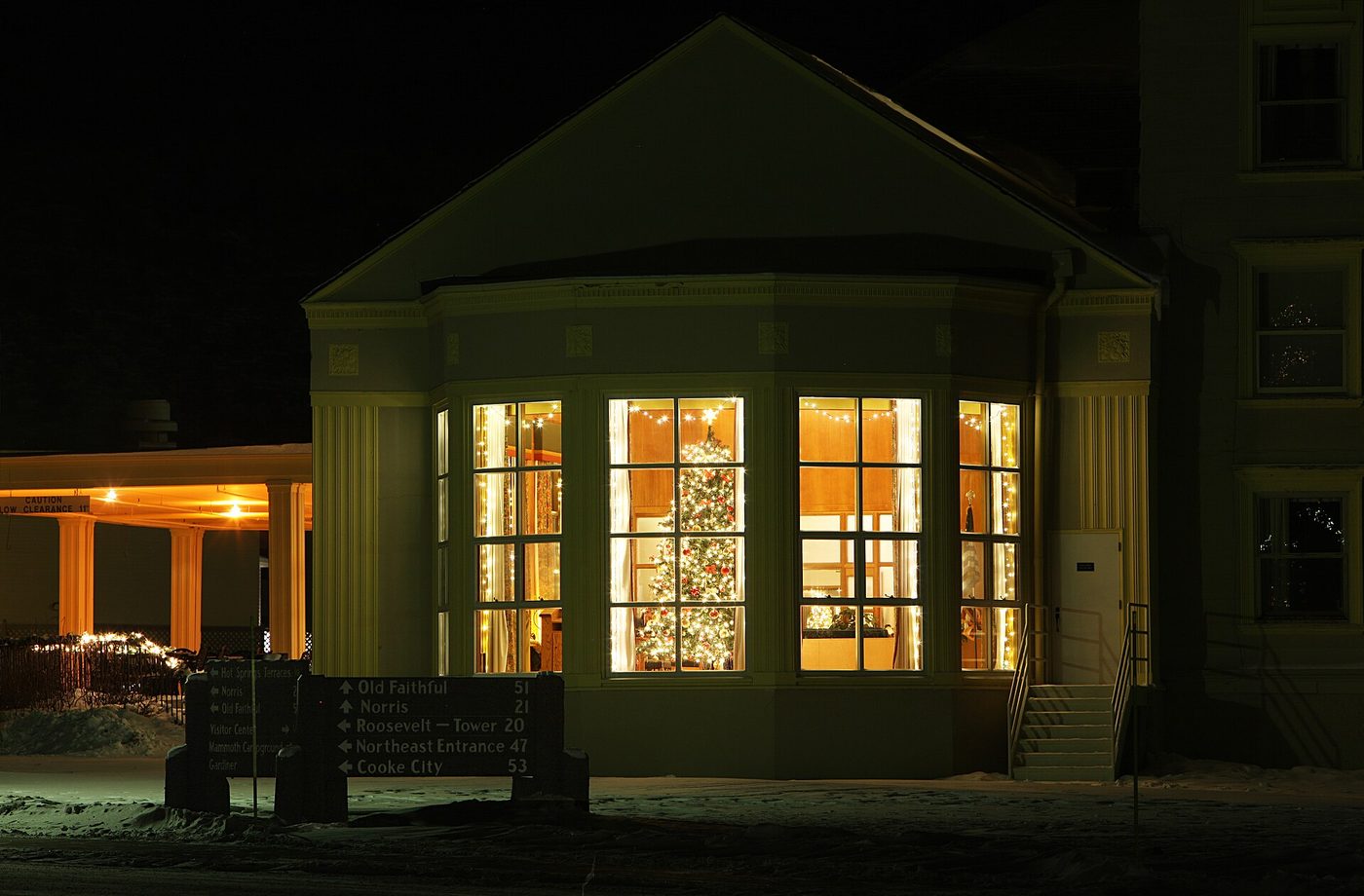 The Mammoth Hot Springs Hotel entrance glowing at night with a Christmas tree in the window