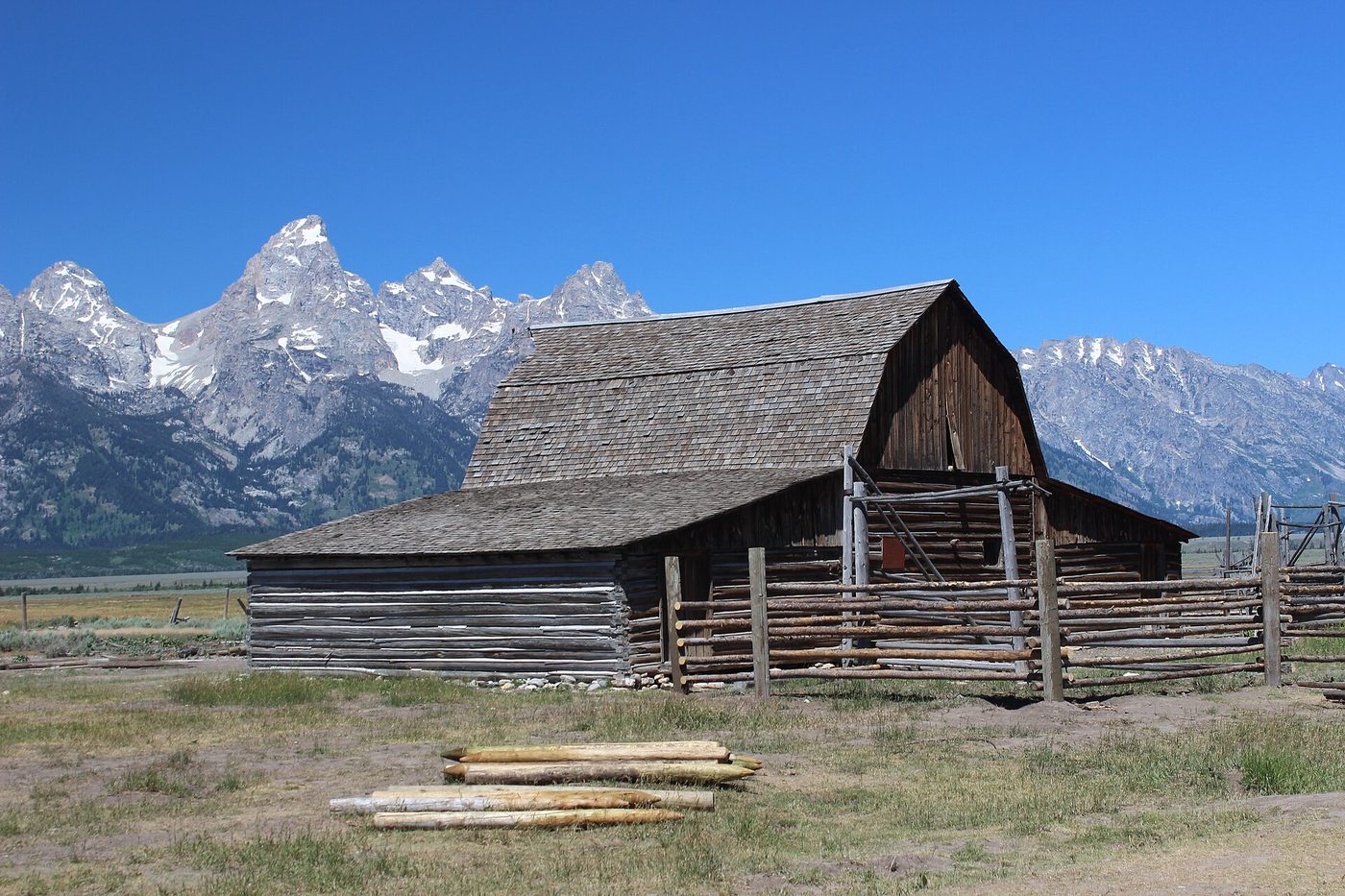 Weathered log barn and corral fence with the Teton peaks behind
