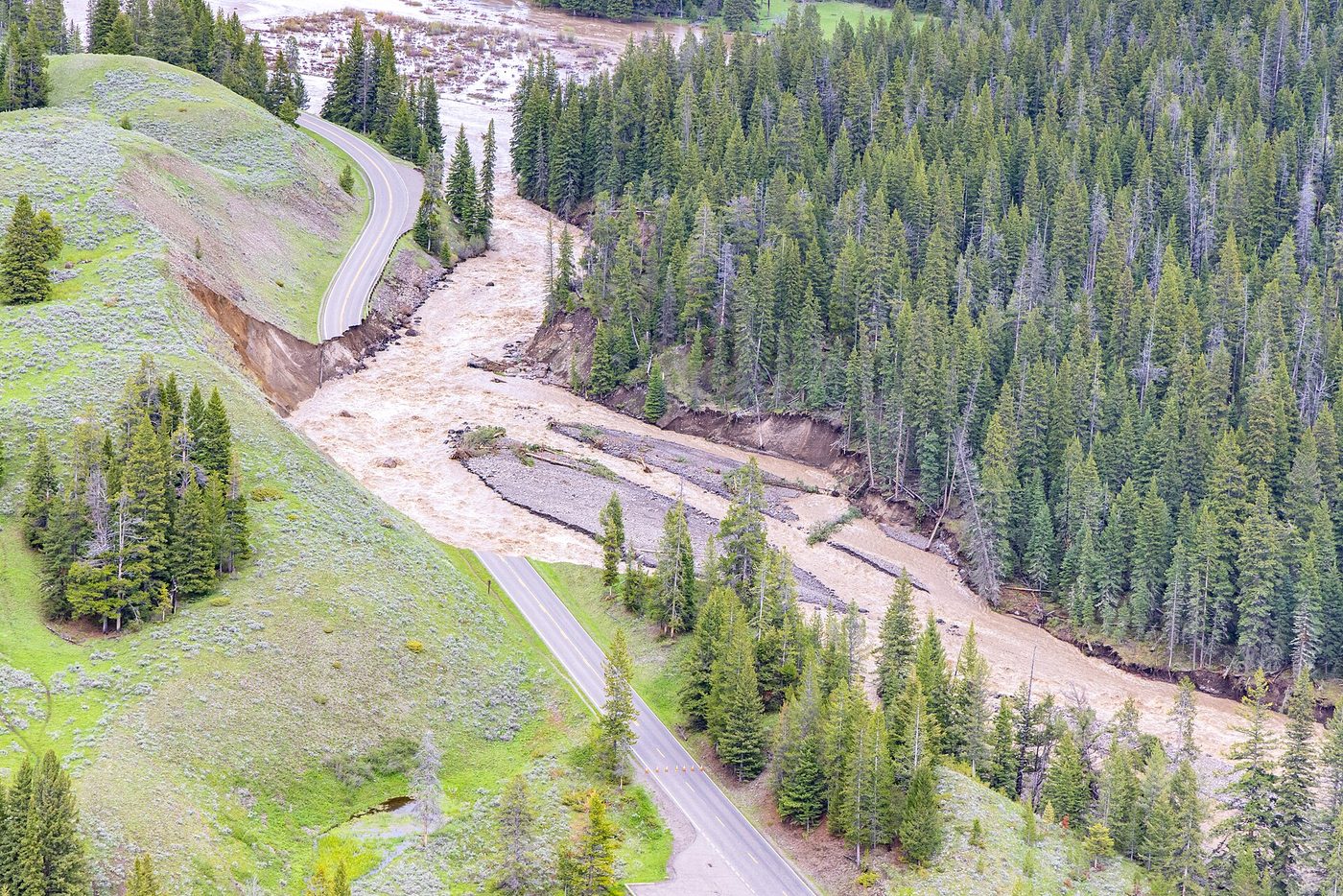 Aerial view of a road washed out by a flooded creek in a forested valley