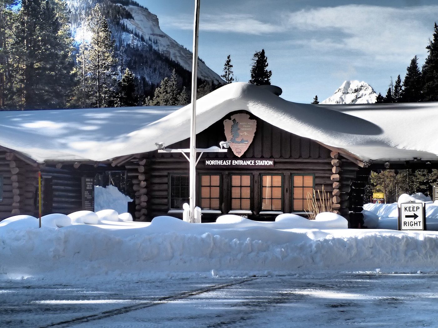 The log-built Northeast Entrance Station under deep snow with plowed banks either side