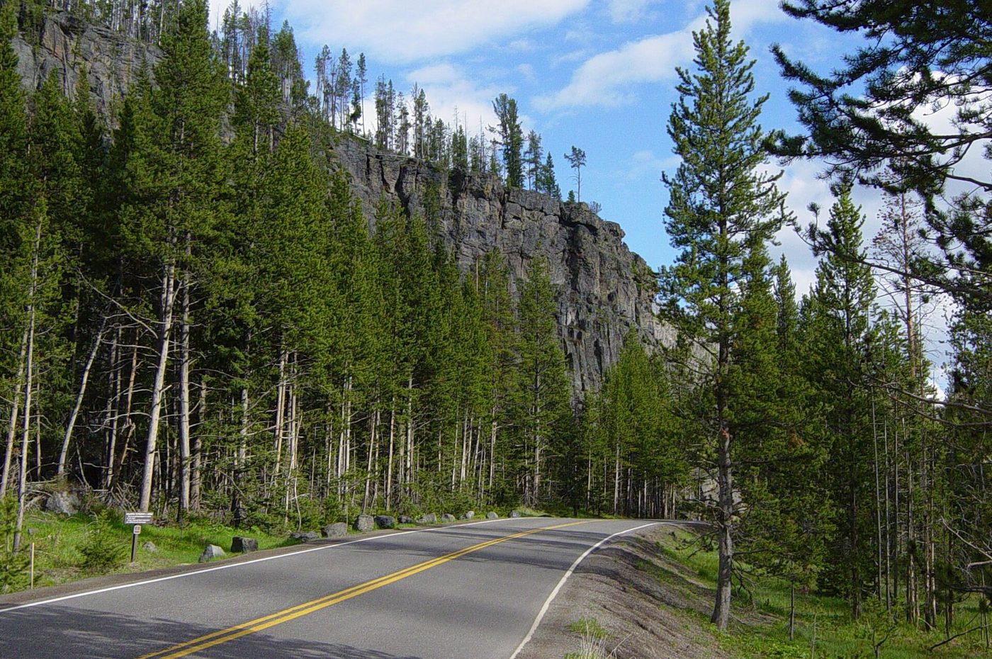 The dark rock face of Obsidian Cliff rising beside the park road