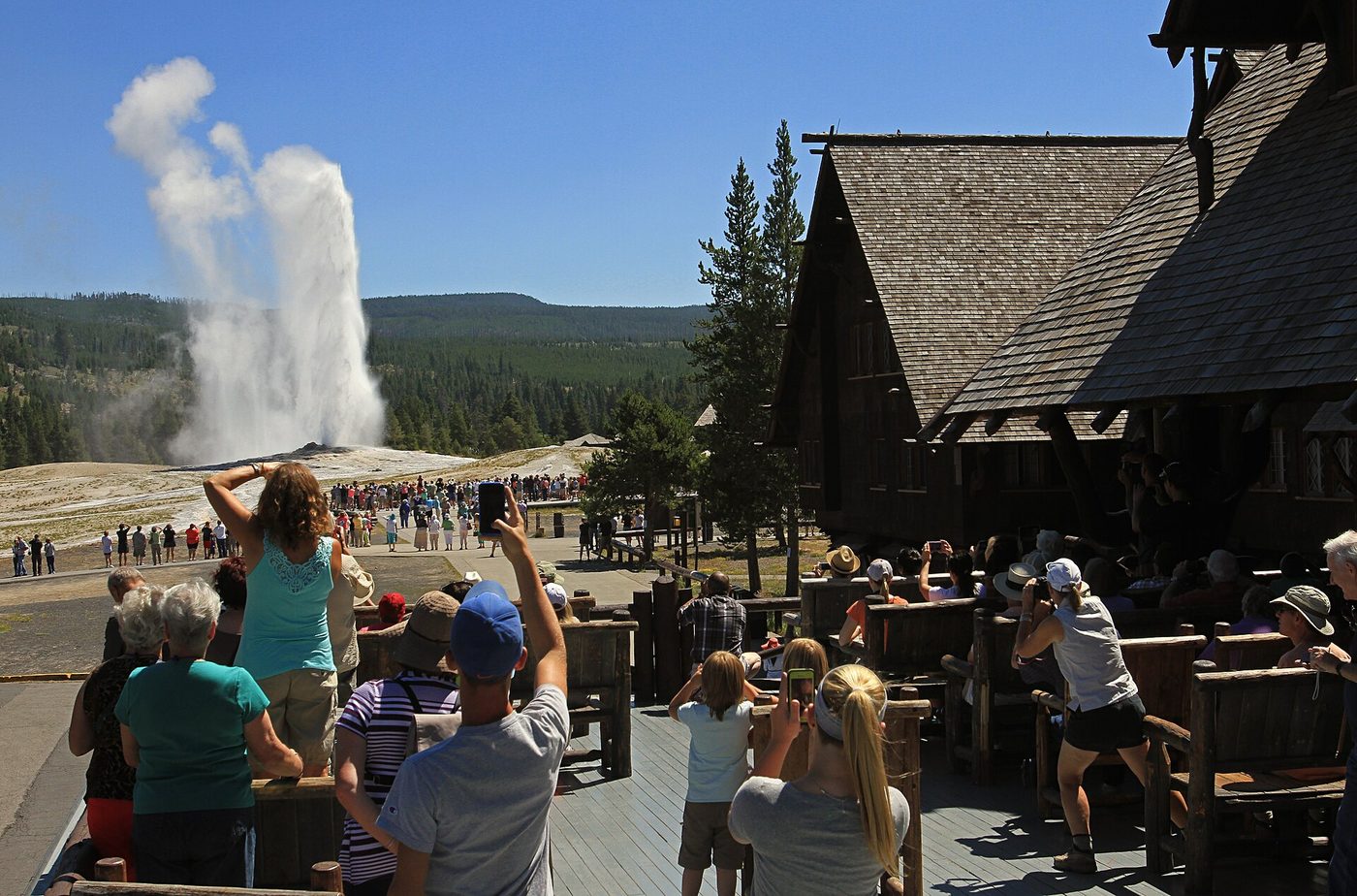 Crowds of visitors on the Old Faithful Inn balcony and the boardwalk beyond, photographing an eruption of Old Faithful