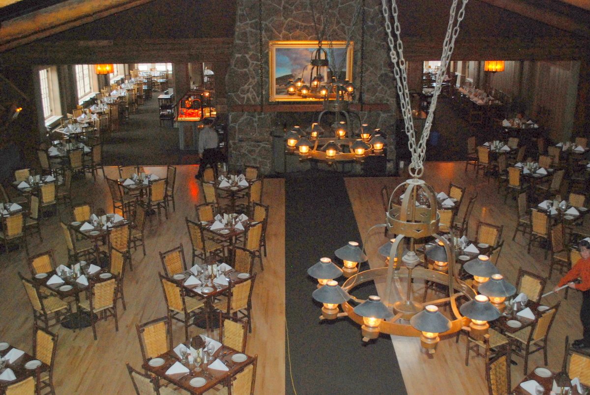 Tables set under wrought-iron chandeliers in the log-walled dining room