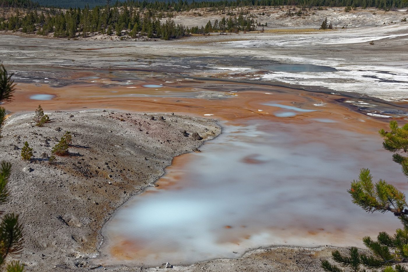 Milky blue pools and rust-orange runoff channels across the white floor of Porcelain Basin
