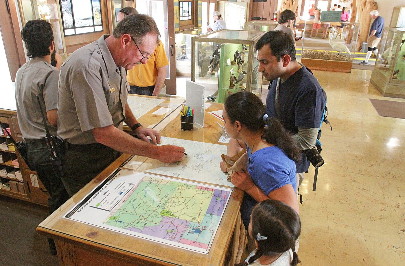 Rangers pointing out routes on a park map to a family at a visitor center desk