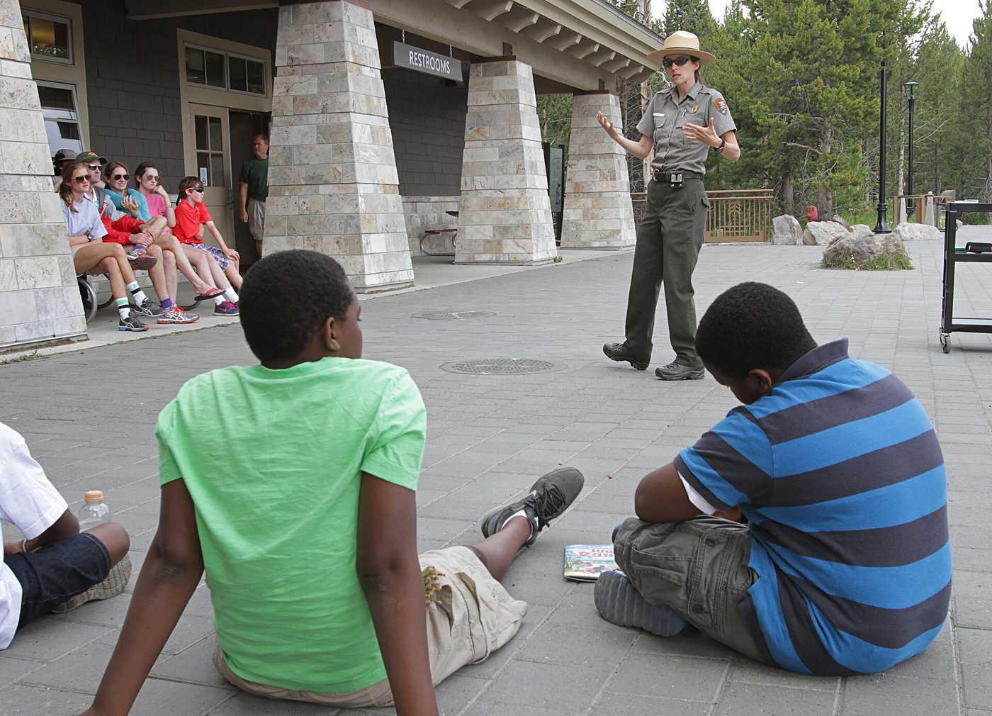 Children and adults sitting on steps listening to a ranger outside the Old Faithful visitor center