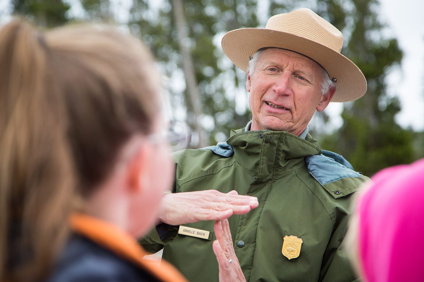 A park ranger crouching to talk with a child at an outdoor program