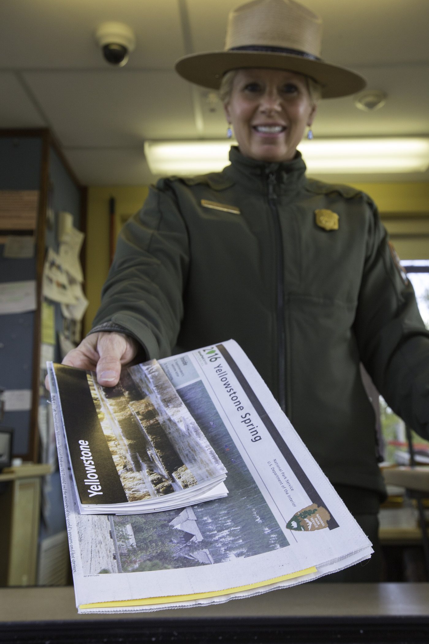 A park ranger in uniform handing a Yellowstone newspaper and map through an entrance booth window