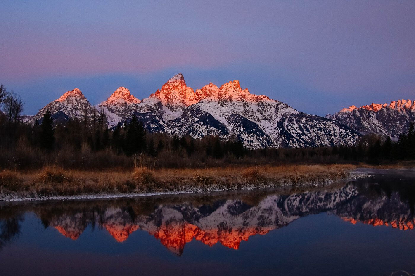 Pink alpenglow on the Teton peaks reflected in still water at Schwabacher Landing