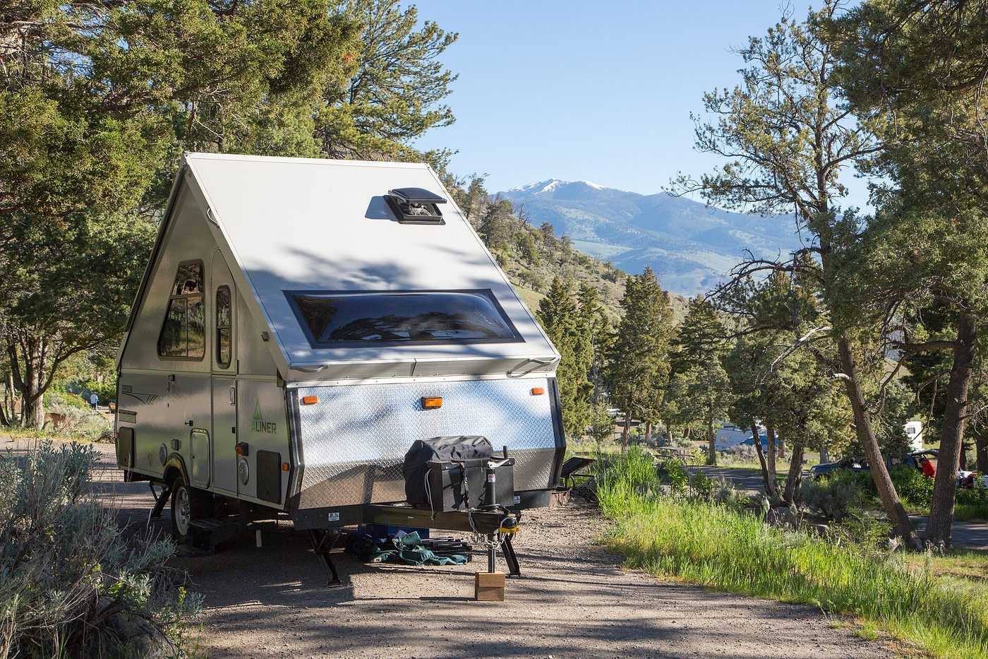 A small aluminium travel trailer parked at a campsite with mountains beyond