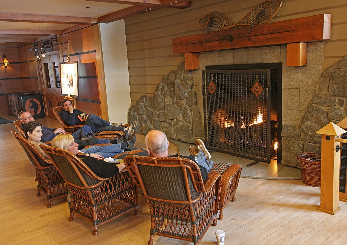 Guests relaxing in wicker chairs by the stone fireplace in the Old Faithful Snow Lodge