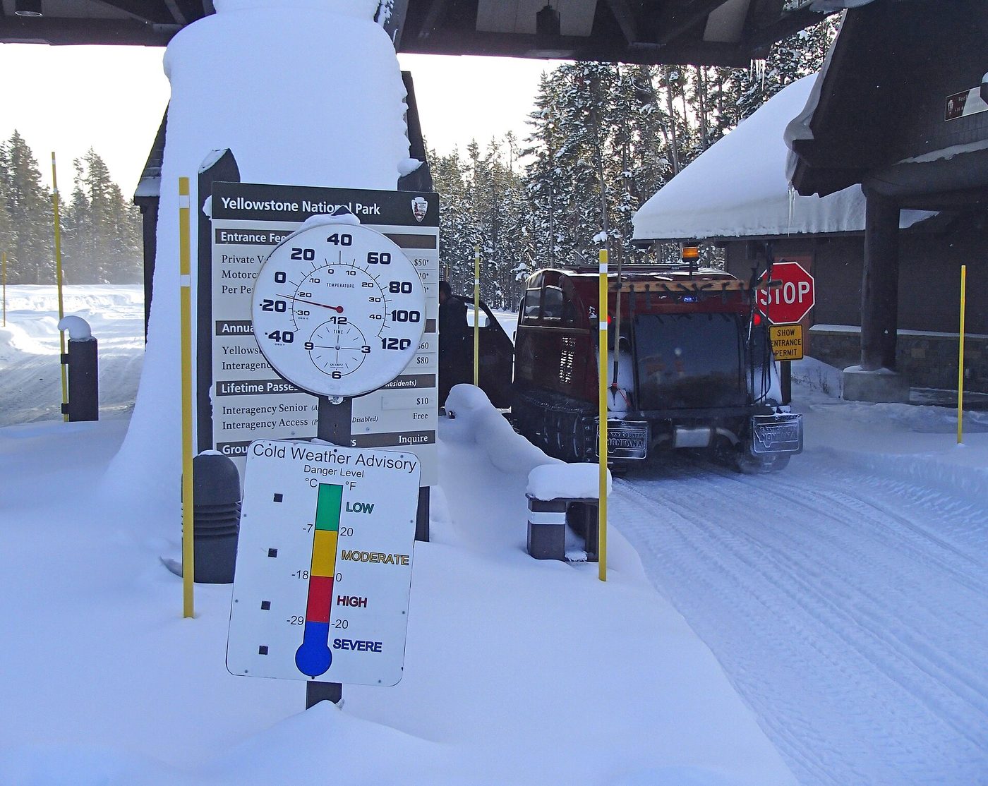A tracked snowcoach at the West Entrance station beside a cold weather advisory sign