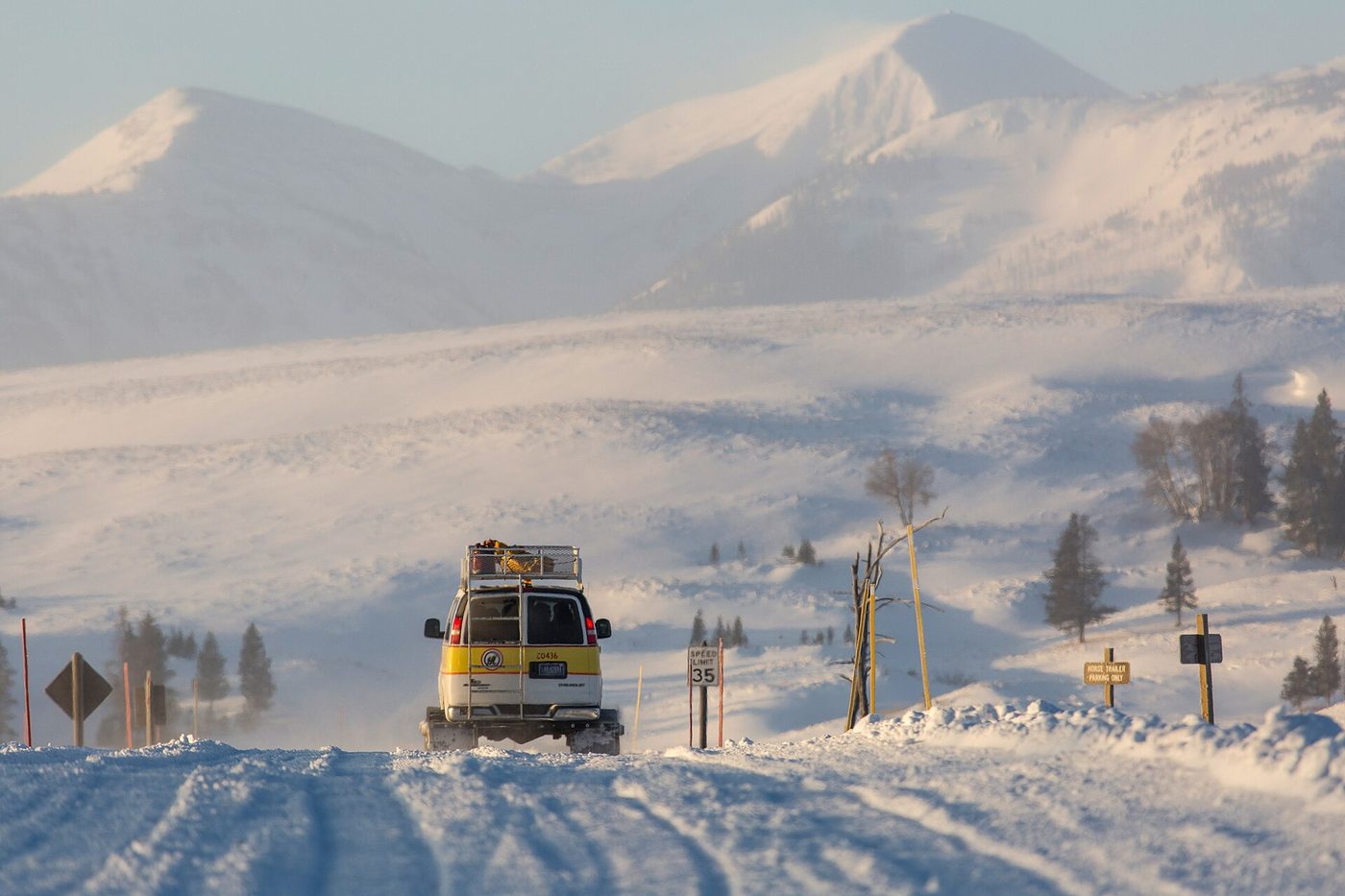 A tracked snowcoach van driving along a snow-covered road on Swan Lake Flat with white mountains behind