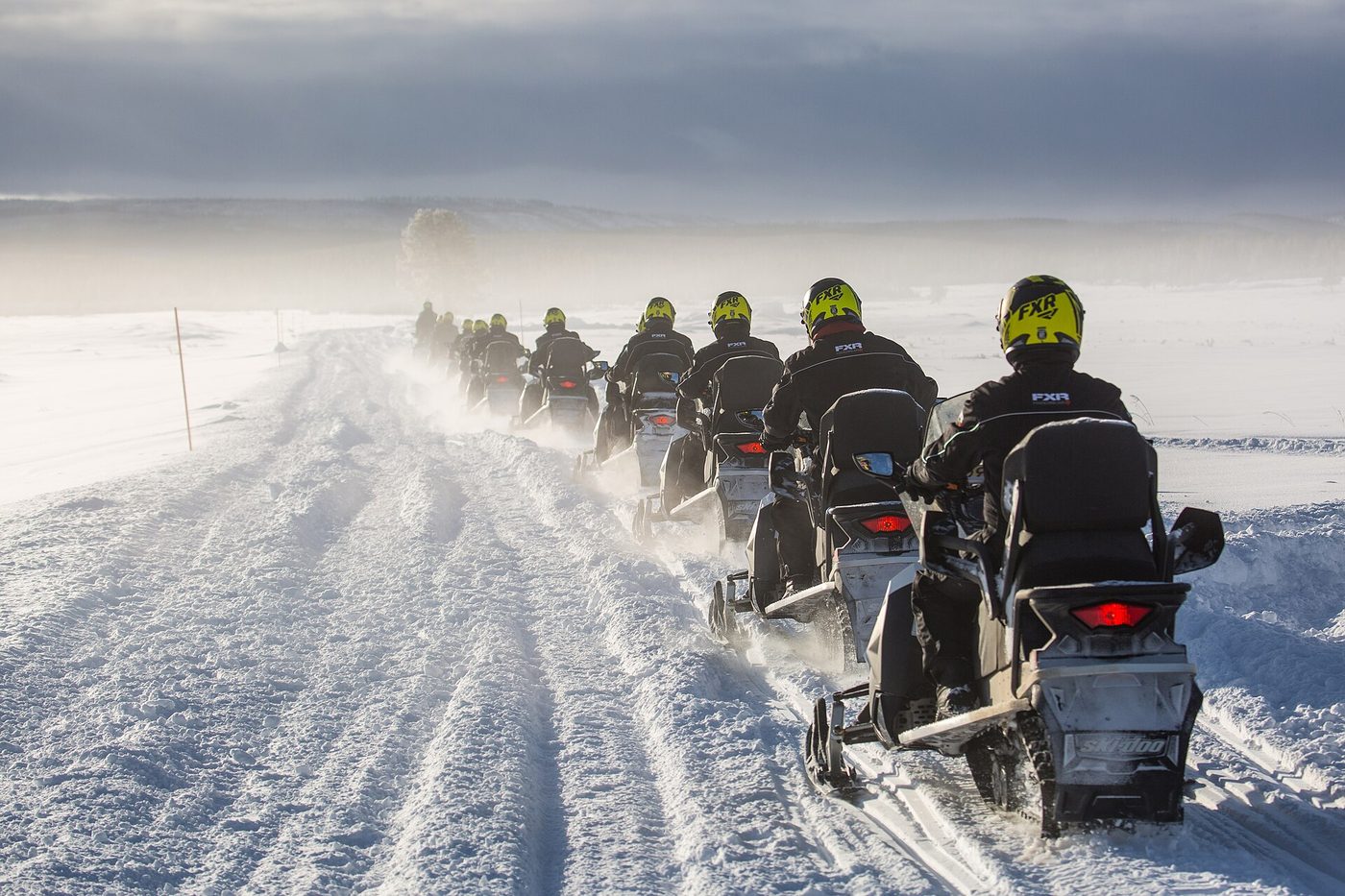 A line of guided snowmobiles crossing windblown Swan Lake Flat