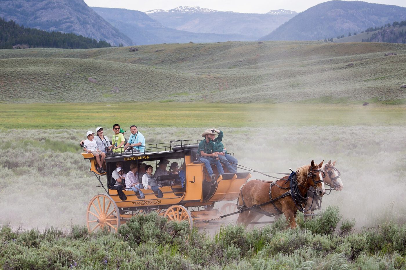 Horse-drawn stagecoach full of passengers kicking up dust across a sagebrush valley