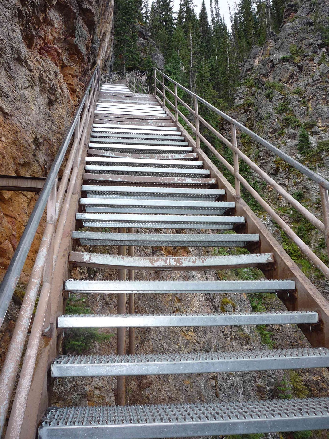 Long steel staircase with railings descending a steep canyon wall