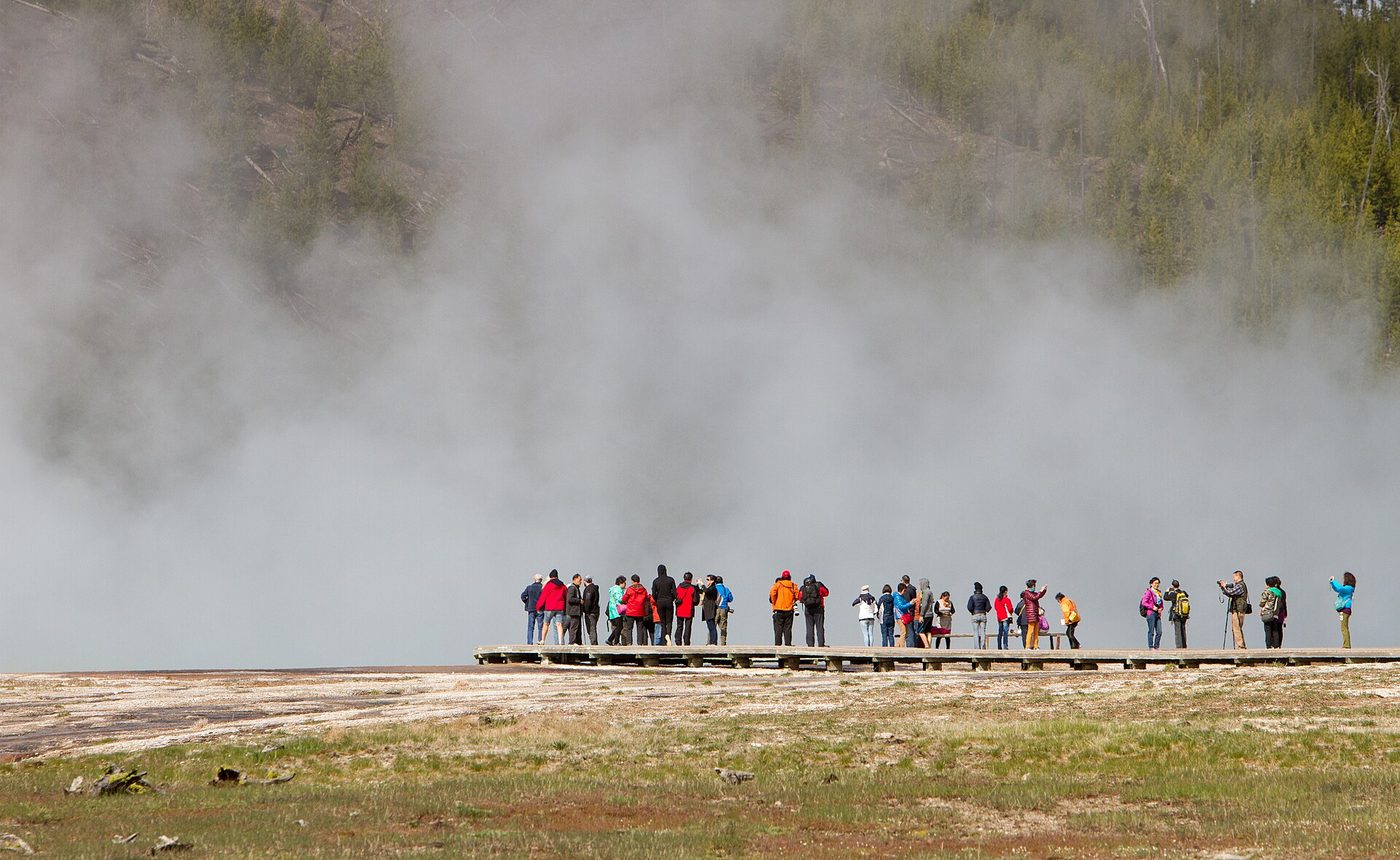 A line of visitors walking the boardwalk across the steaming runoff of Grand Prismatic Spring