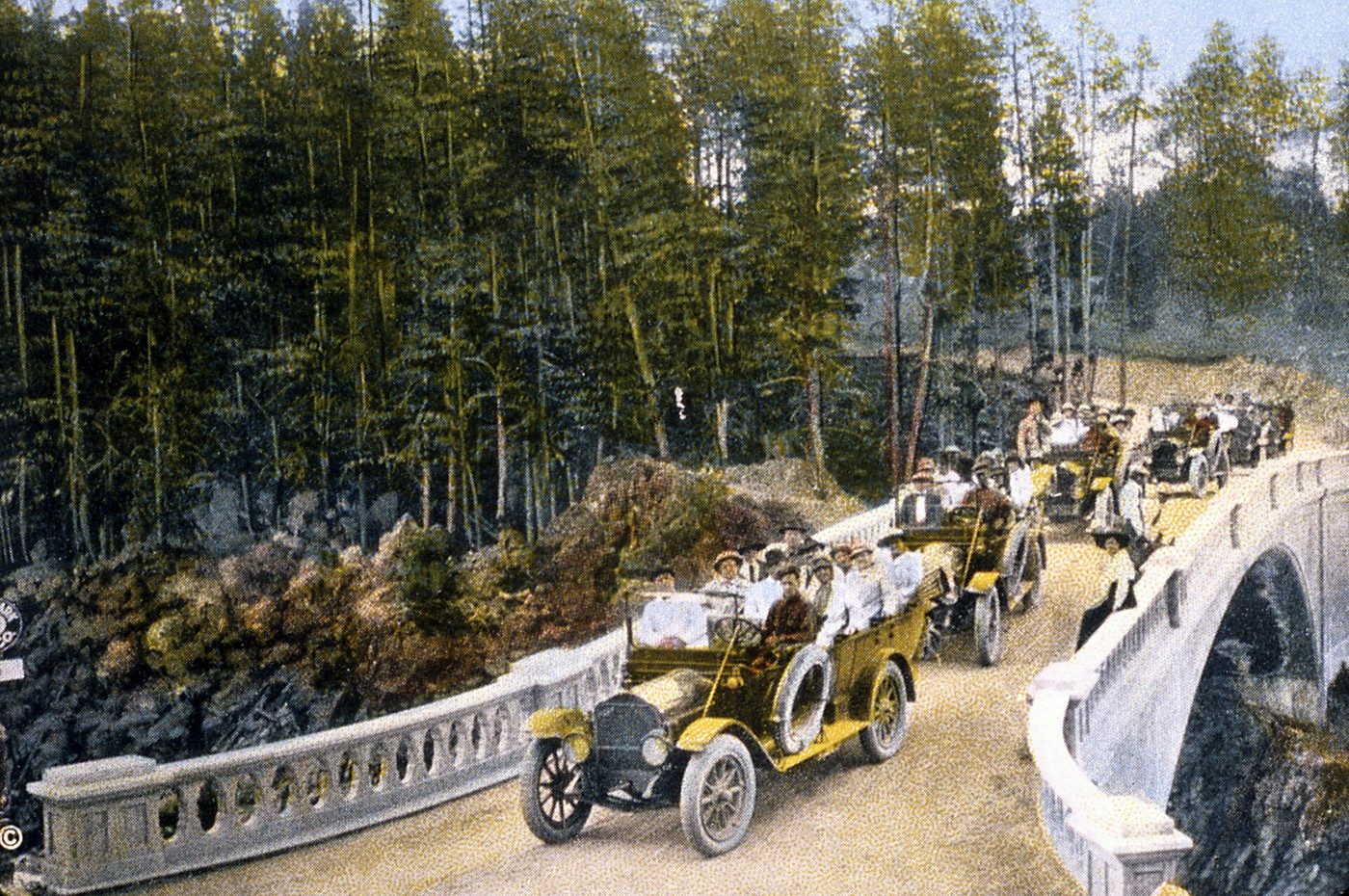 Hand-colored early photo of open touring cars crossing a stone-railed bridge