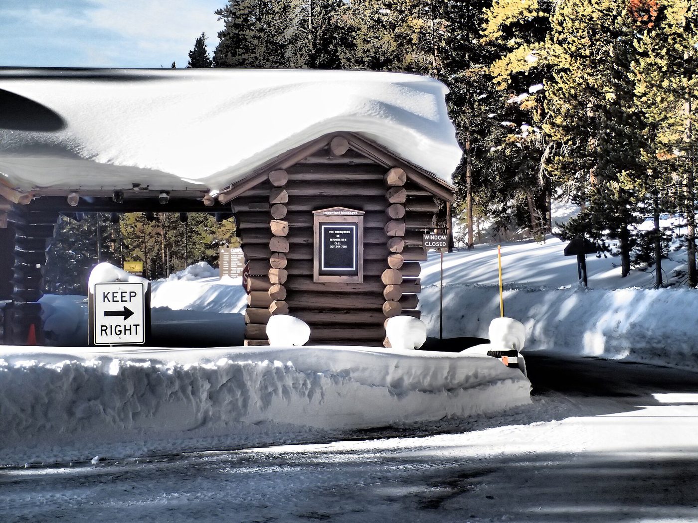 A log entrance booth with a Keep Right sign, banked with snow at a Yellowstone gate