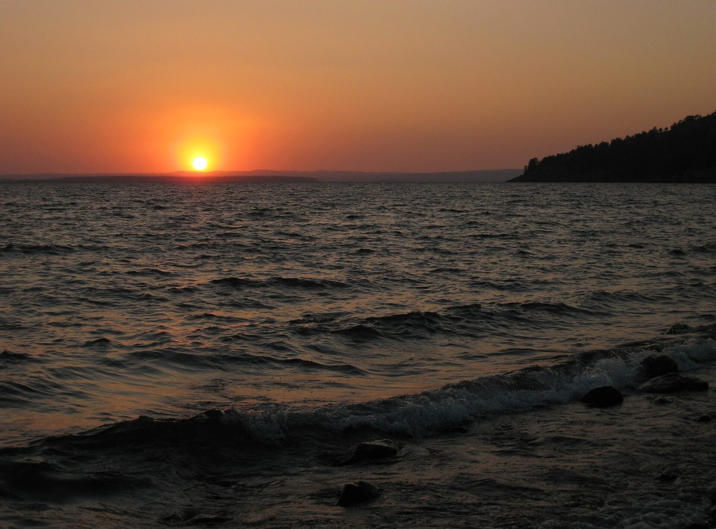An orange sun setting over the choppy water of Yellowstone Lake