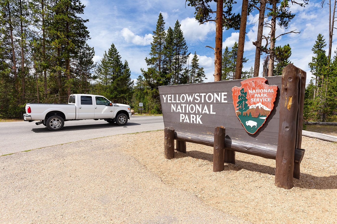 Wooden Yellowstone National Park boundary sign with the arrowhead emblem beside a road